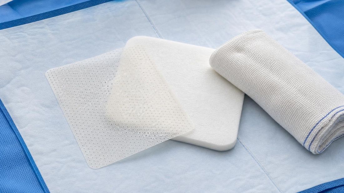 Tanki perforirani kontaktni sloj i sekundarna upijajuća obloga na sterilnoj kliničkoj podlozi, bez rane, teksta, logotipa ili identiteta pacijenta.