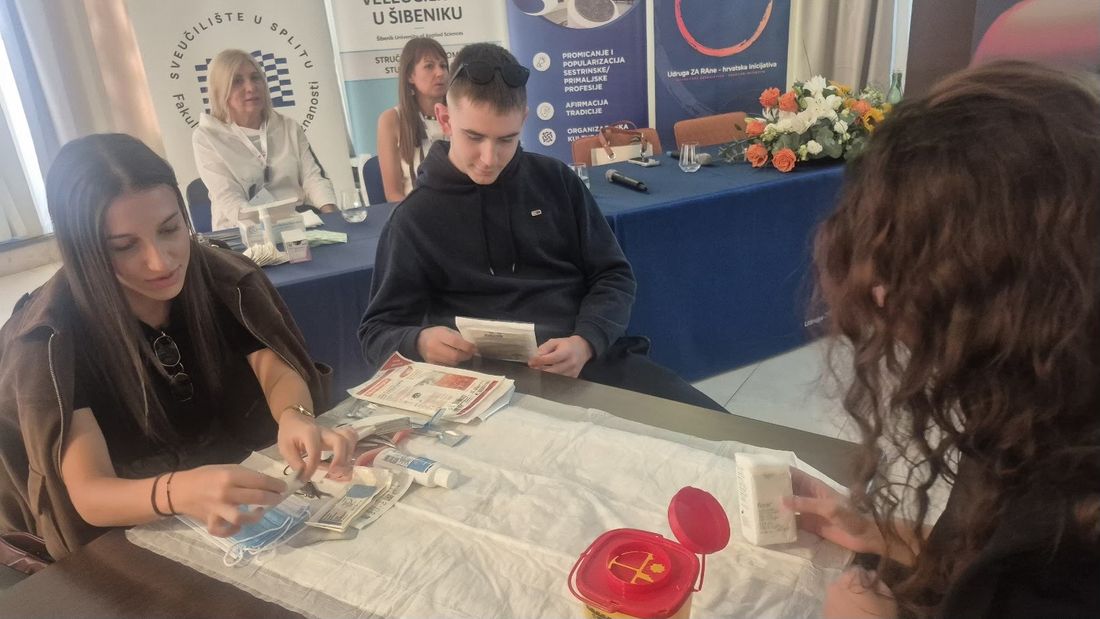 Učenici na praktičnoj radionici razgledavaju pribor i materijale za previjanje rana na stolu sa sterilnom podlogom
